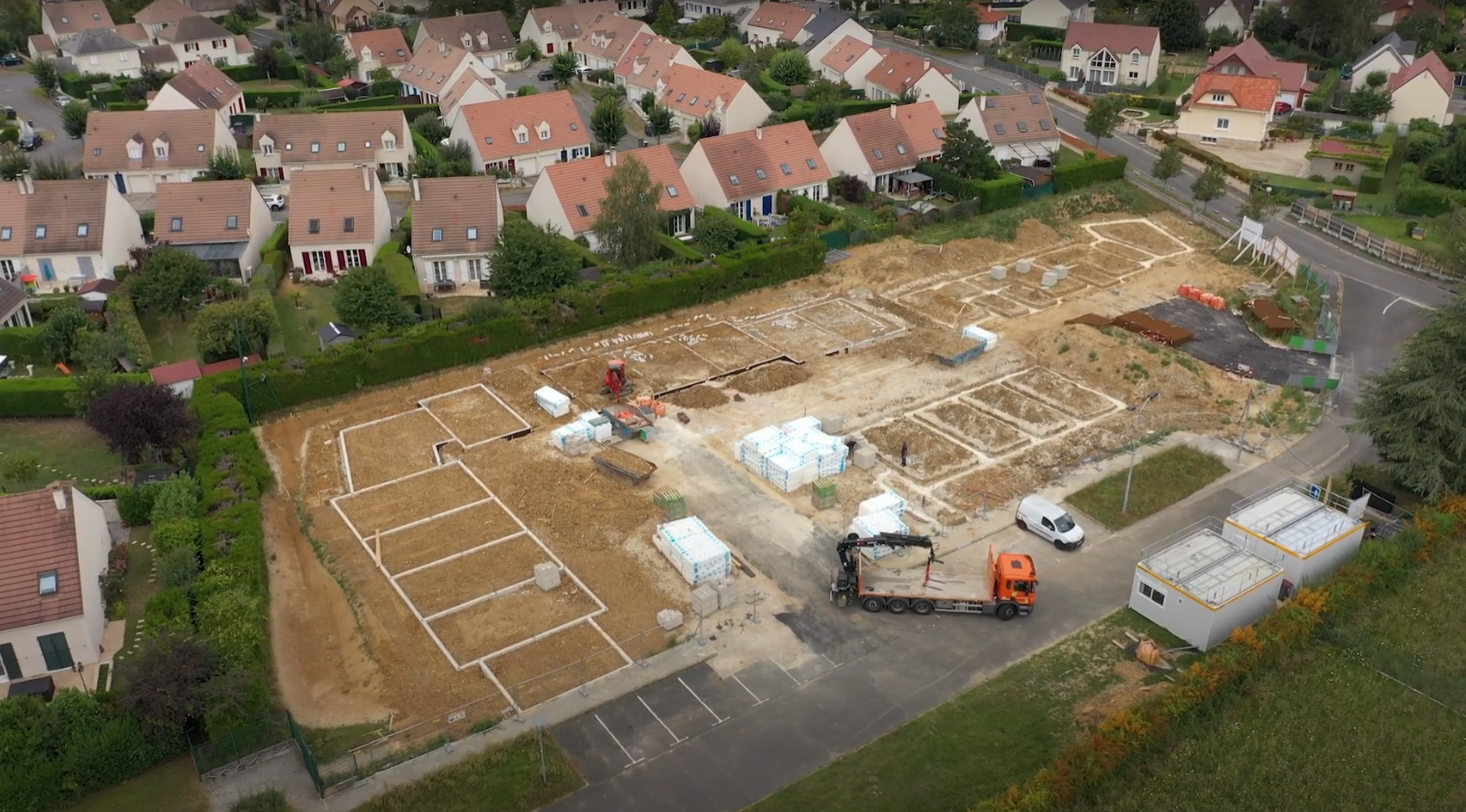 Image aérienne d'un site de construction avec maisons et voitures.