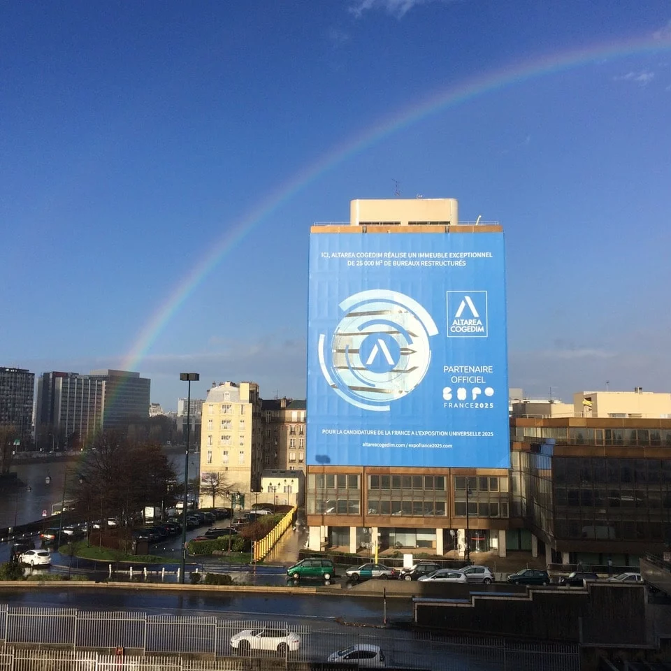 Un arc-en-ciel surplombe un grand panneau publicitaire devant un bâtiment.